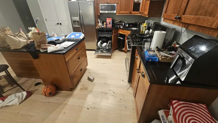 Photo of the real kitchen: a cherry-wood island with a bar stool, bags on the counter and clothes on the floor